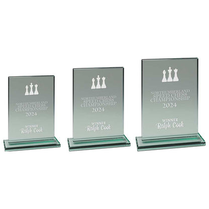 Three glass awards with engraved text and chess piece symbols on a white background