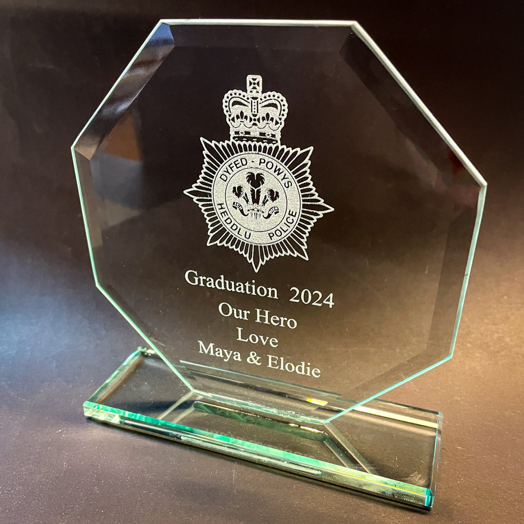 Glass award with engraved text and logo on a dark background