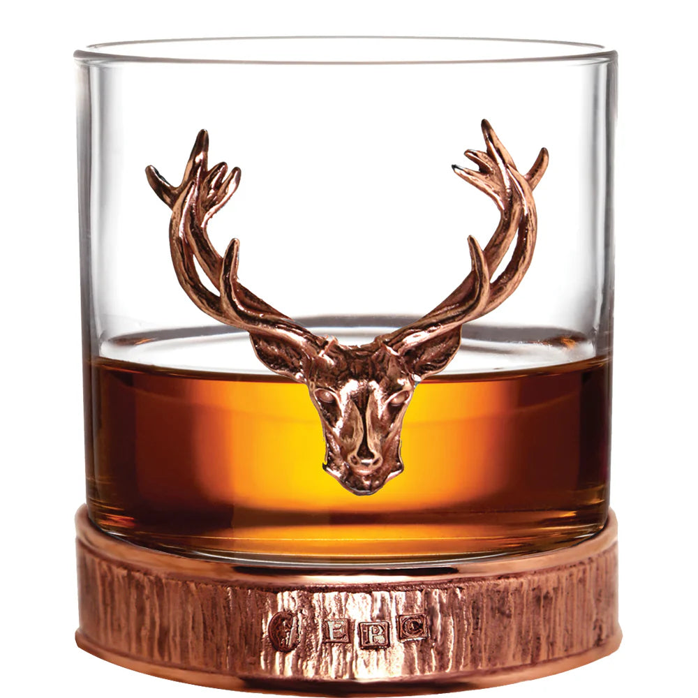 Whiskey glass with a bronze deer head design on a white background